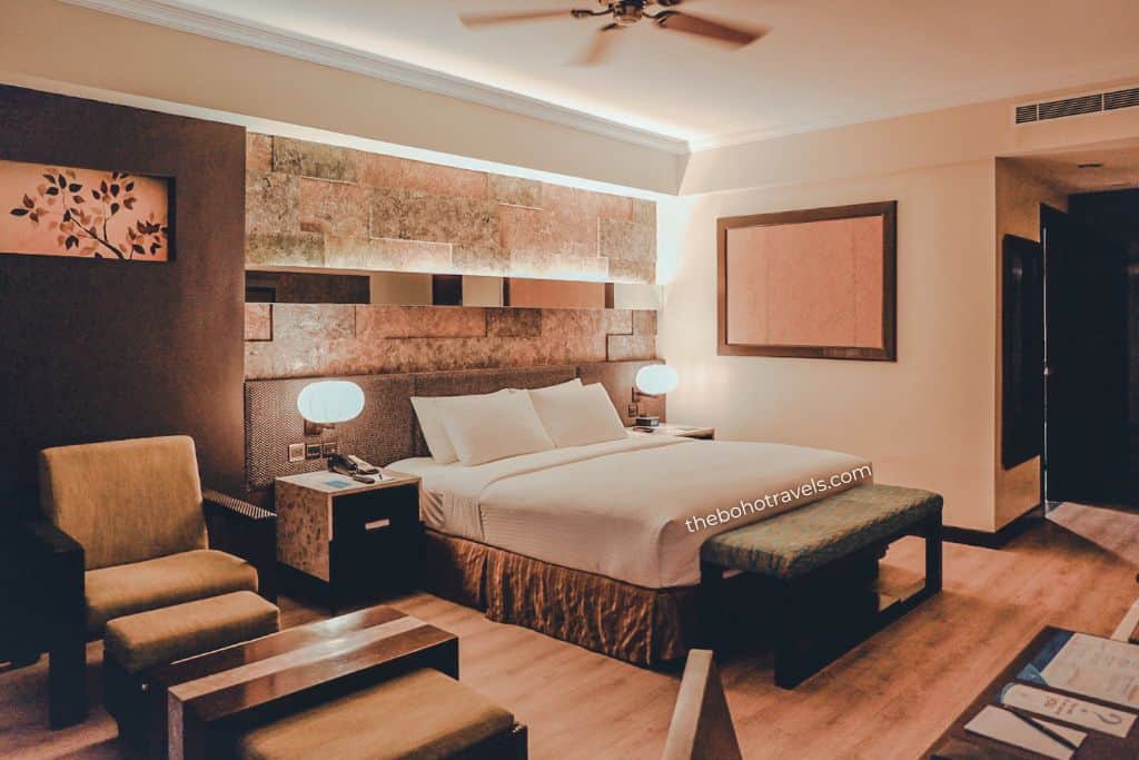 A modern hotel room features a large bed, bedside lamps, comfortable seating, and warm lighting. Staying in a comfortable resort provides a convenient base for exploring the many things to do in Bohol.