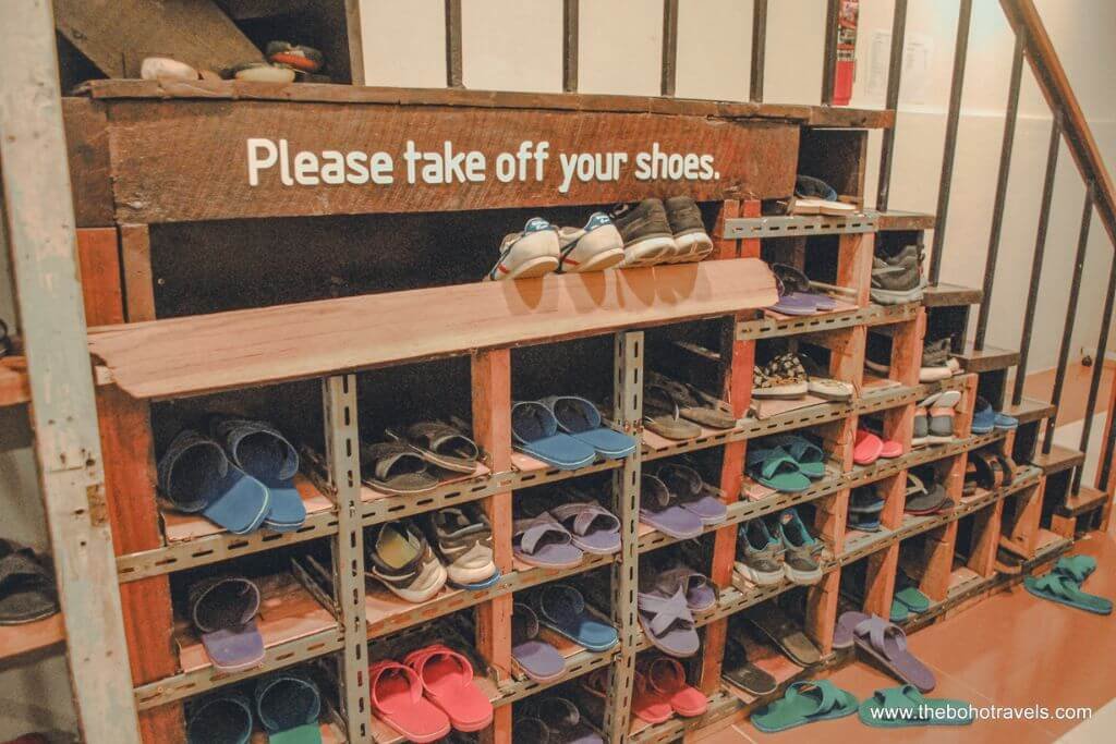 Shoe rack at the entrance of a Chiang Mai hostel with a sign reading Please take off your shoes.