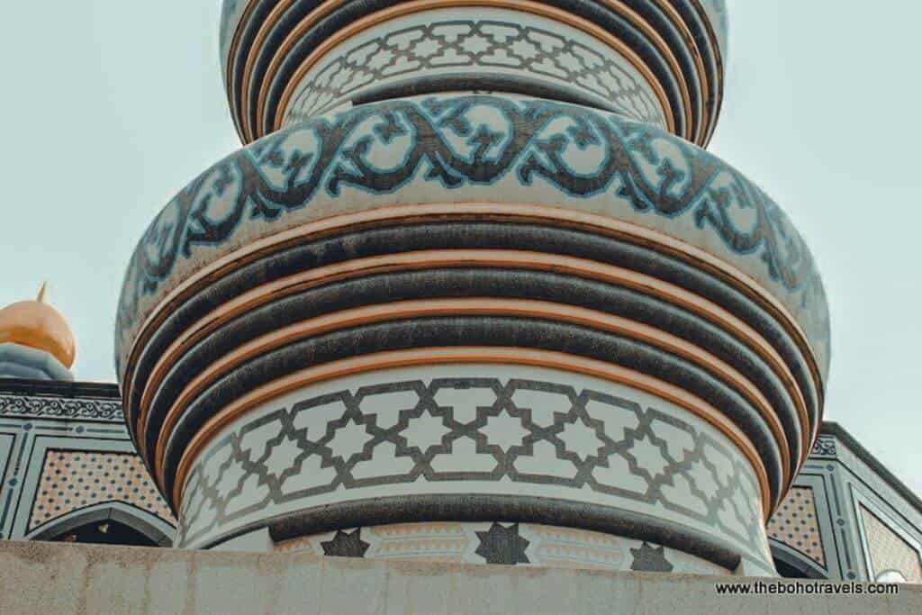 A close view of a mosque's large golden domes and crescent finial rises above intricate blue and white decorative tilework. The architectural details show the ornate Islamic design found throughout Brunei.