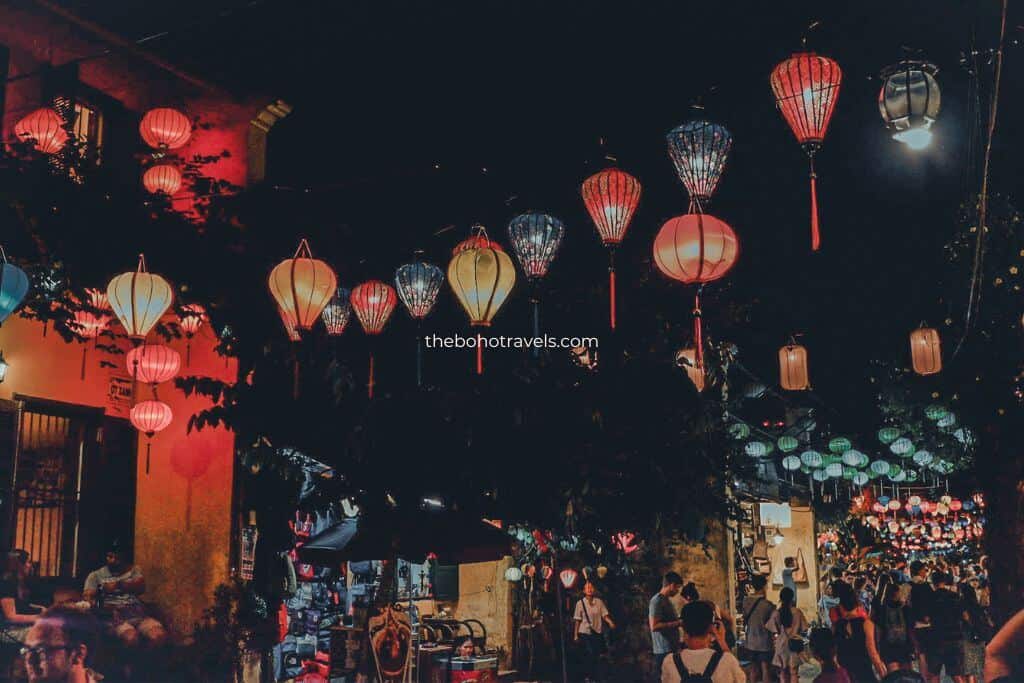 Colorful paper lanterns hang above a lively street market at night as visitors walk beneath the glowing lights. The festive atmosphere captures the vibrant nightlife and cultural experiences travelers can discover in a Southeast Asia travel guide.