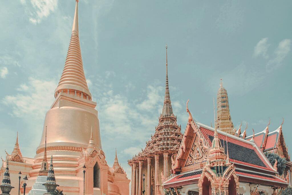 Ornate temple buildings with golden spires, colorful tiled roofs, and intricate architectural details stand beneath a bright blue sky. The grand religious complex showcases the rich history, craftsmanship, and iconic landmarks travelers can explore in a Southeast Asia travel guide.