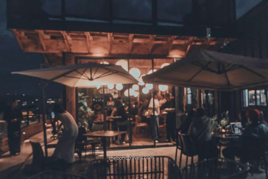 Outdoor rooftop seating filled with guests enjoying food and drinks under large umbrellas and warm hanging lights at night. The lively atmosphere makes it a memorable spot for where to drink in Baguio.