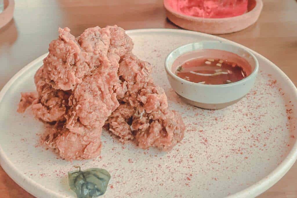 Crispy fried chicken is served on a large ceramic plate with a bowl of dipping sauce and a small dollop of green condiment. The savory bar food pairs well with cocktails at a speakeasy in Baguio.