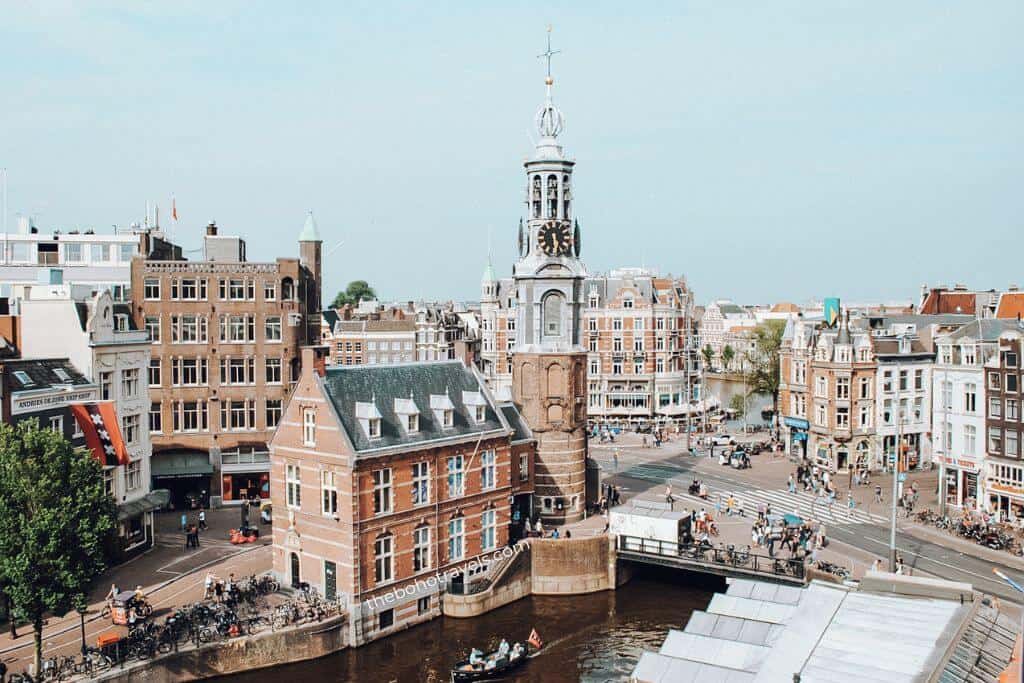 Historic canal houses and the Munttoren clock tower overlook a busy canal and bridge in Amsterdam on a clear day. This classic cityscape highlights the charm of Amsterdam as a popular stop in a Europe travel guide.