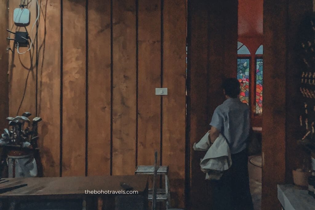 A guest walks through a wooden doorway into a dimly lit bar with stained glass accents, creating a hidden and exclusive feel. The discreet entrance captures the charm of speakeasies in Baguio and hints at a unique place for visitors wondering where to drink in Baguio.