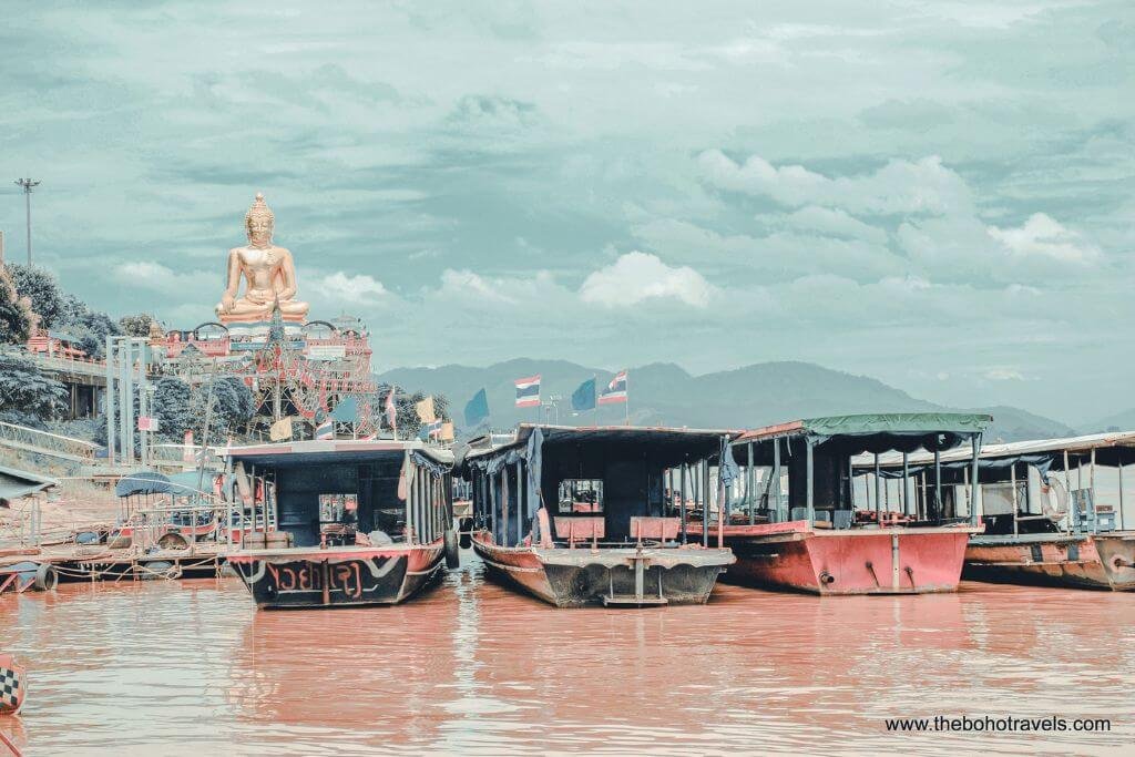 Boats docked on the Mekong River at the Golden Triangle with a golden Buddha in the background, seen on a Chiang Rai day trip from Chiang Mai.