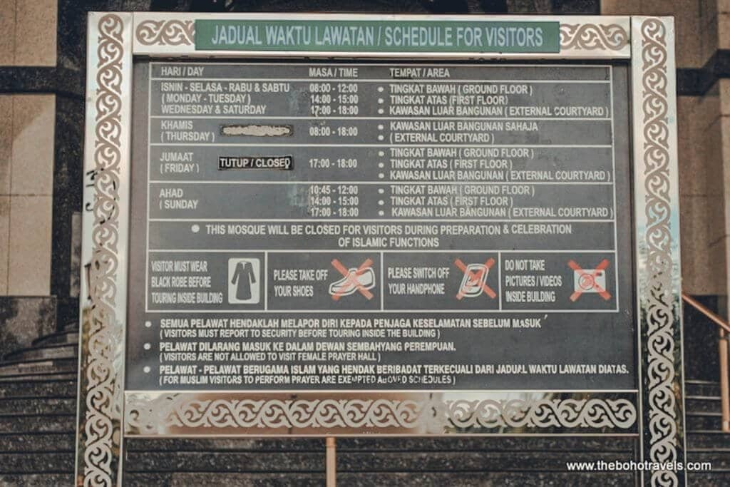 A visitor information sign displays mosque visiting hours and rules in Malay and English. The sign provides practical visiting information for travelers planning where to stay in Brunei.